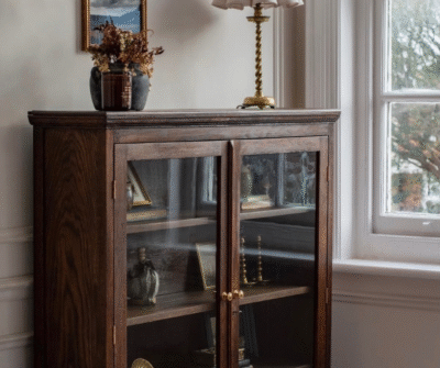 Dark wood cabinet displaying photos and decor pieces inside, with a candle and a lamp placed above the cabinet.