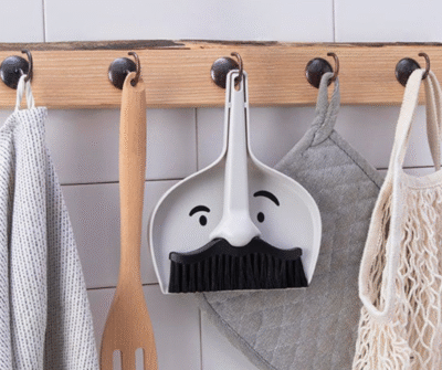 Man with a mustache-shaped hand brush and dustpan set for cleaning kitchen island crumbs.