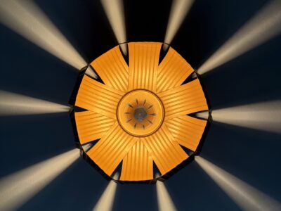 Top-down view of a radiating sunburst light fixture with orange-yellow slats casting dramatic light beams on the ceiling in a Solomons, Maryland home.