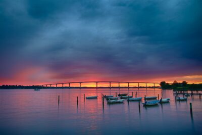 Gov. Thomas Johnson Bridge (MD-4) crossing the Patuxent River at sunset near Solomons, Maryland. Local crabbing and fishing boats are docked on reflective water.